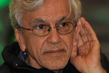 Caetano Veloso com a mão junto ao ouvido como se tentasse escutar a resposta